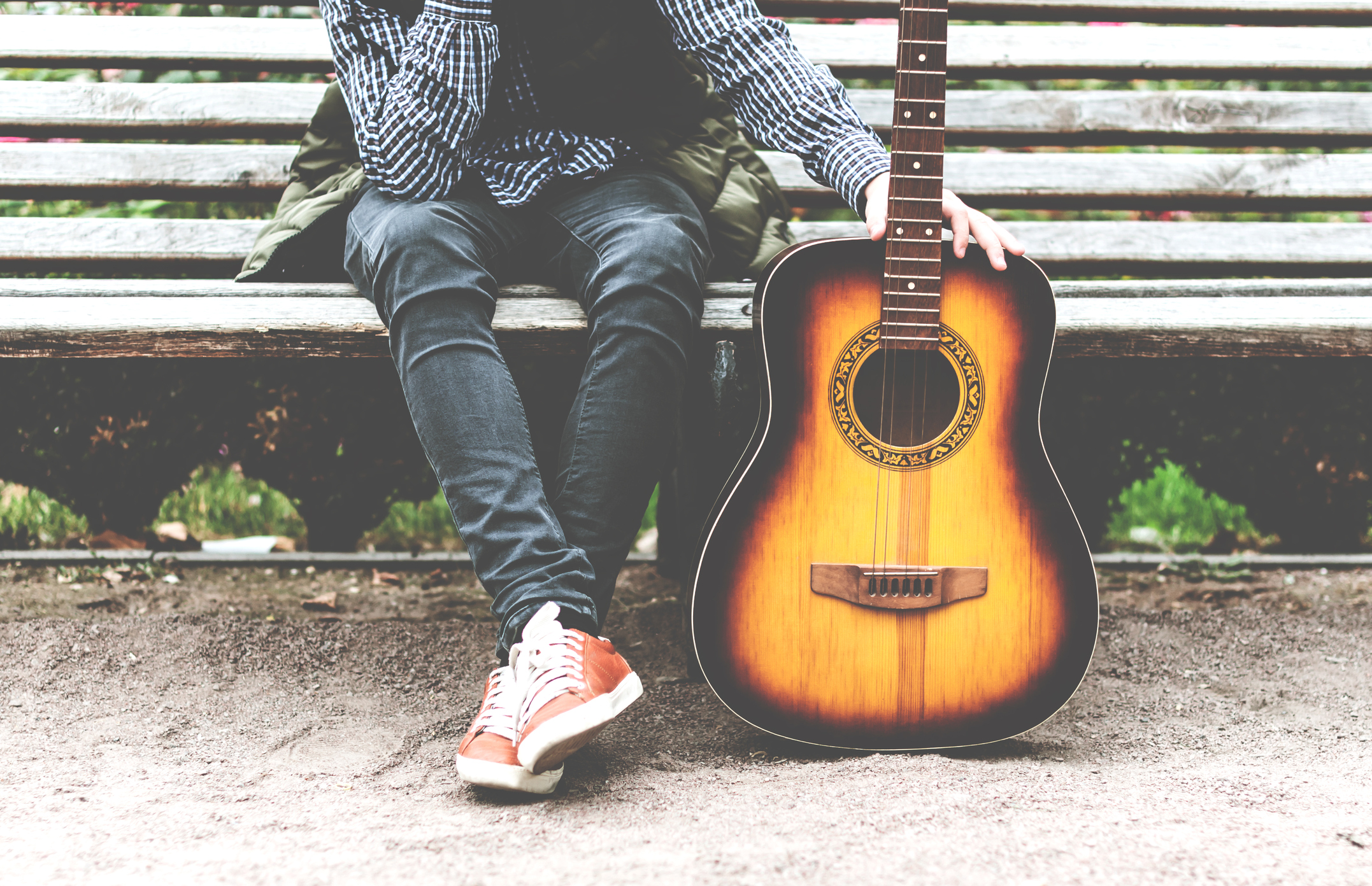 young man sitting in the park on a bench with a guitar